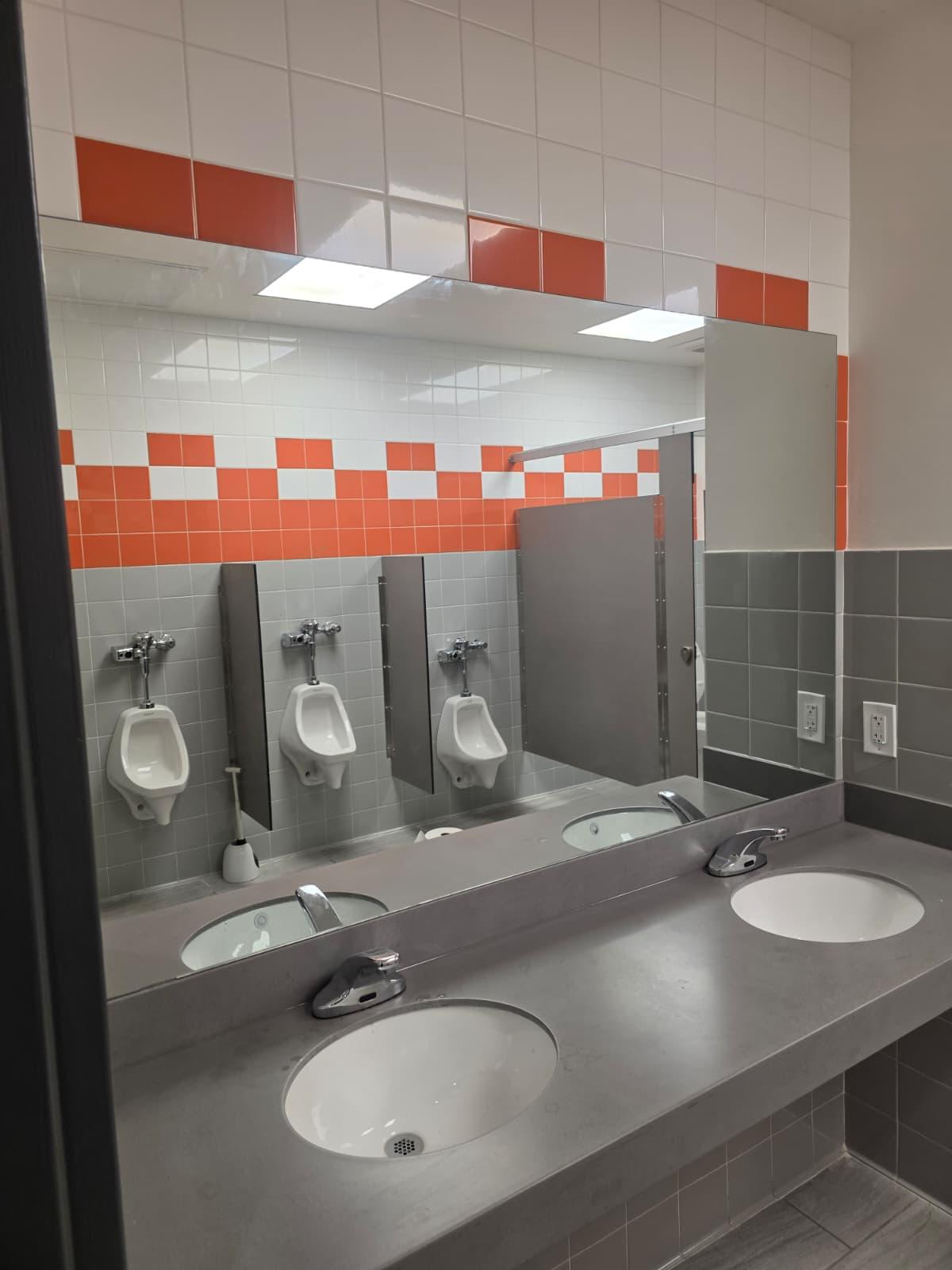 Urinal wall with touchless flush valves, privacy screens, and matching accent tile band.