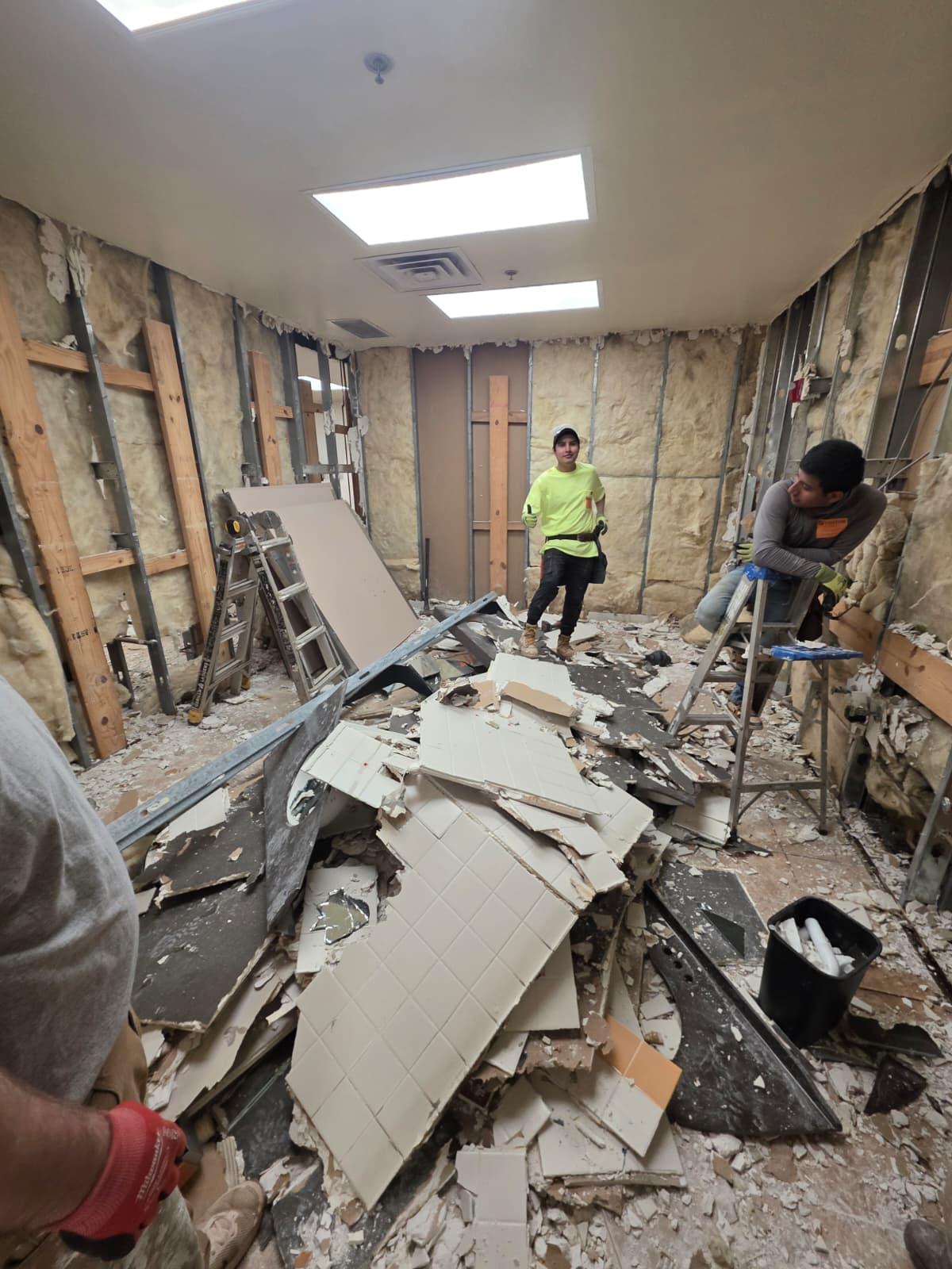 Crew mid-stripout — tile and drywall pulled back to studs and insulation.
