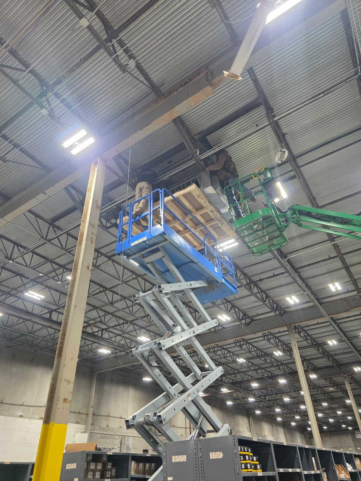 Overhead unit replacement in an active warehouse — crews working from scissor and boom lifts.