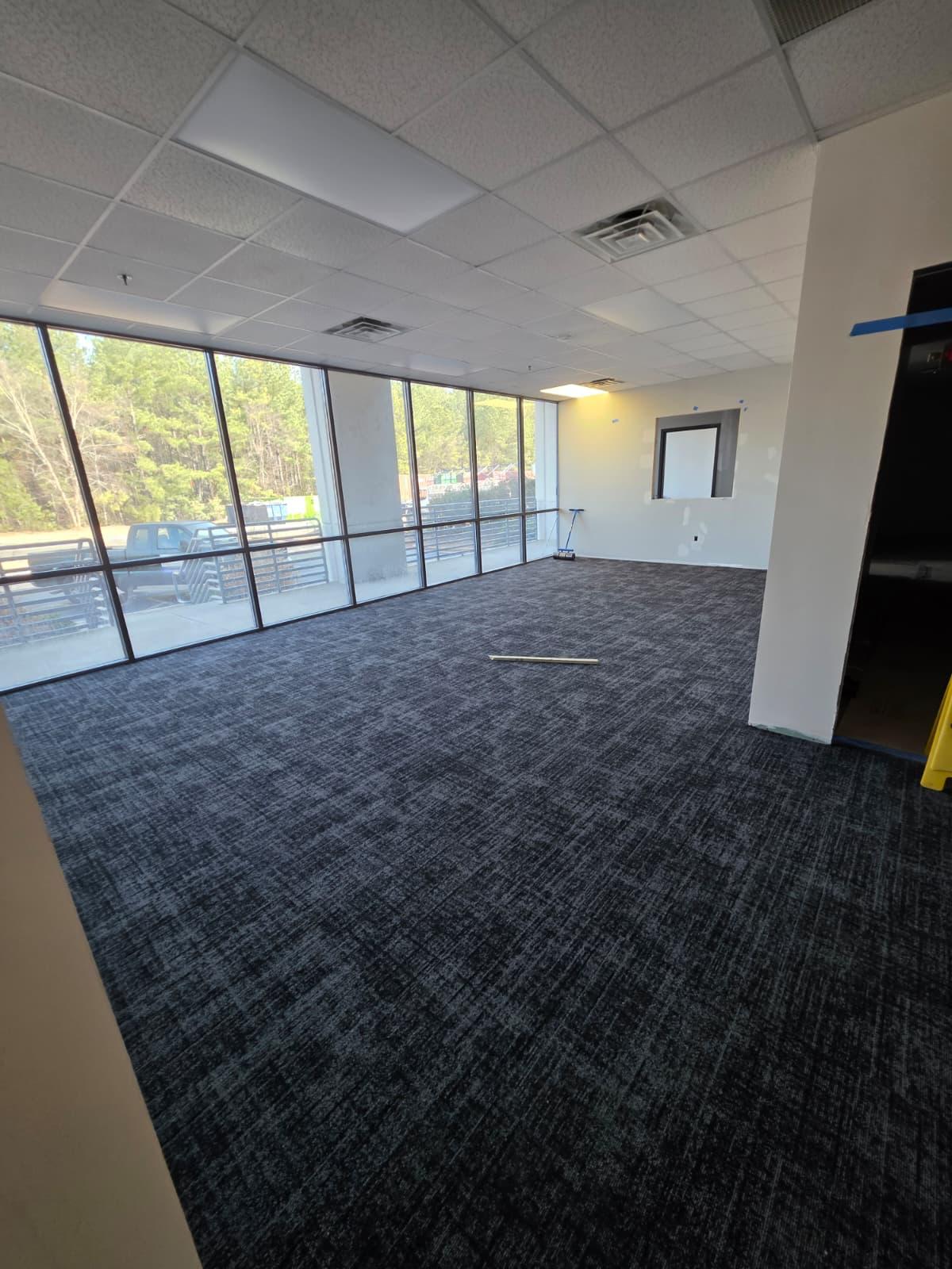 Open work area with fresh carpet tile, ceiling grid, and full glazing — ready for furniture install.
