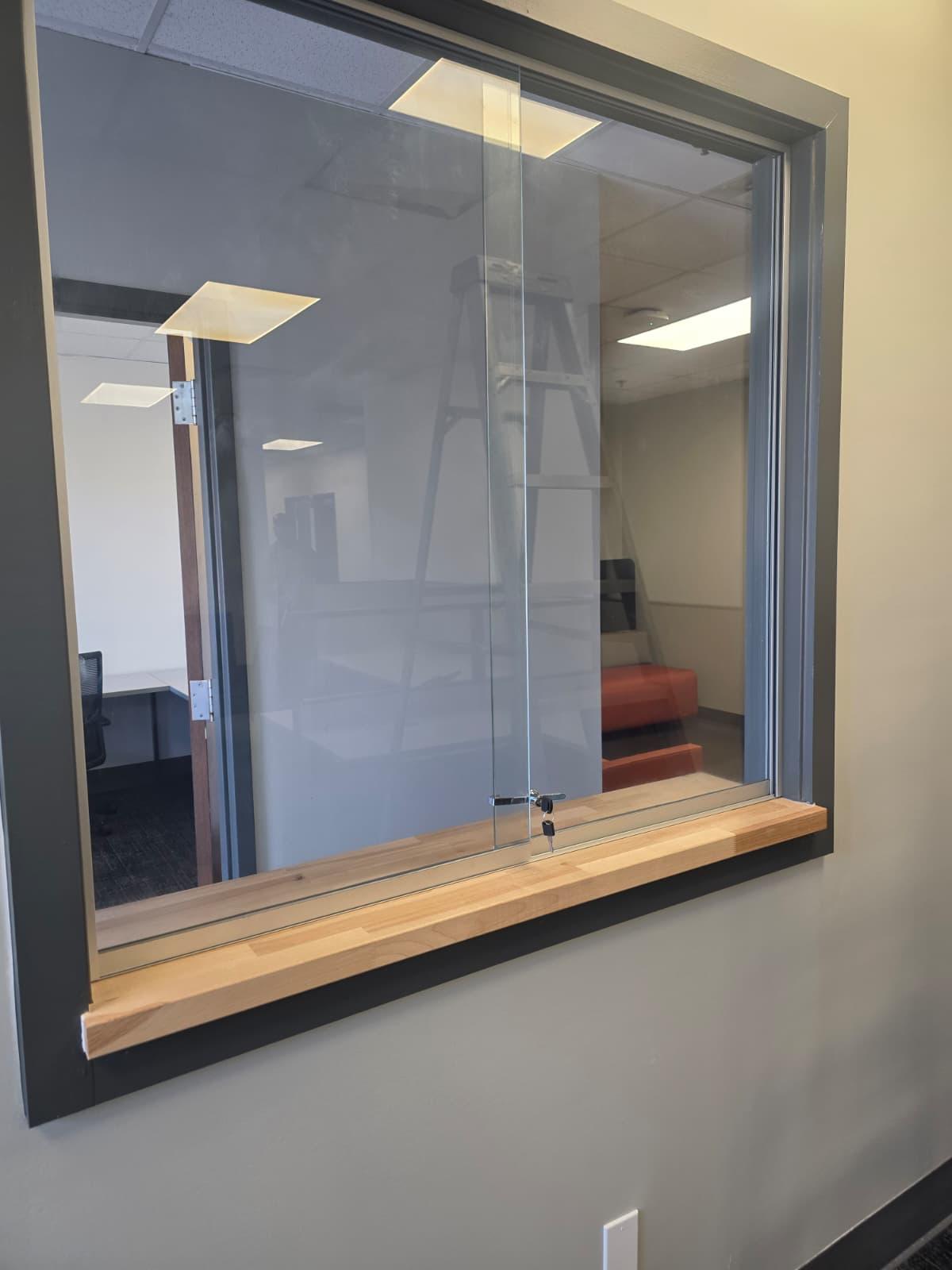 Interior service window with sliding glass, key lock, and solid wood transaction sill.