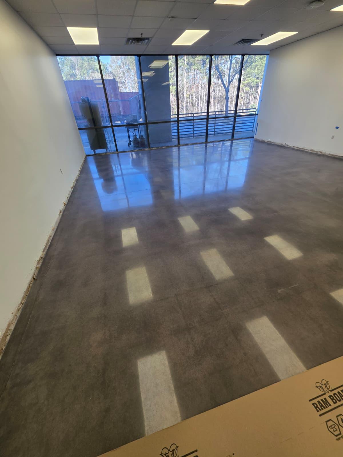 Charcoal-stained polished concrete in a window-front office suite — high gloss with natural mottling.